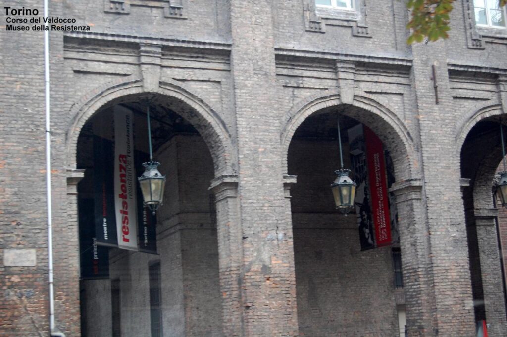 L'ingresso del museo della resistenza di Torino. Primo piano di due portici del porticato del palazzo del museo. sotto uno dei quali si intravede lo stendardo che segna l'ingresso del museo
